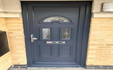 Dark grey front door with decorative glass panels set into a yellow brick wall